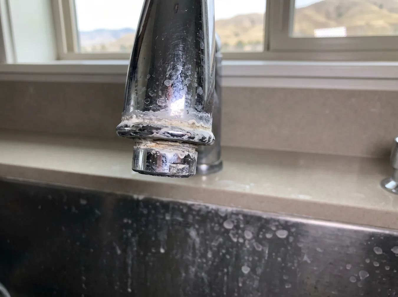 Kitchen faucet crusted with white limescale above a spotted stainless sink