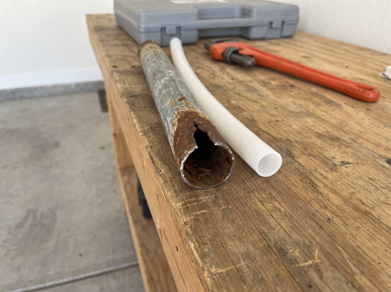 Corroded galvanized pipe cut open beside new white PEX tubing on a workbench