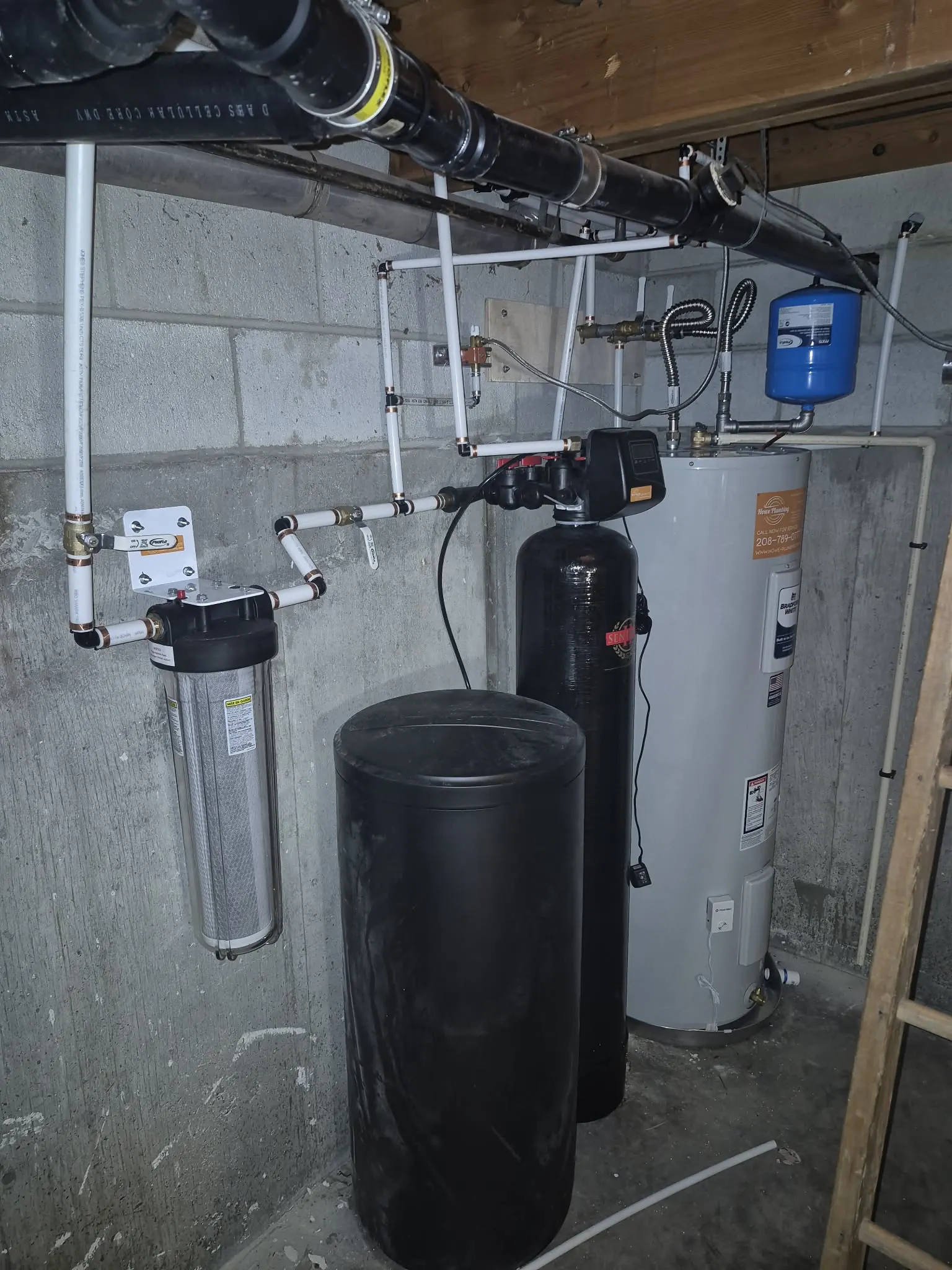 Water softener, brine tank and whole-house filter installed by Howe Plumbing beside a water heater